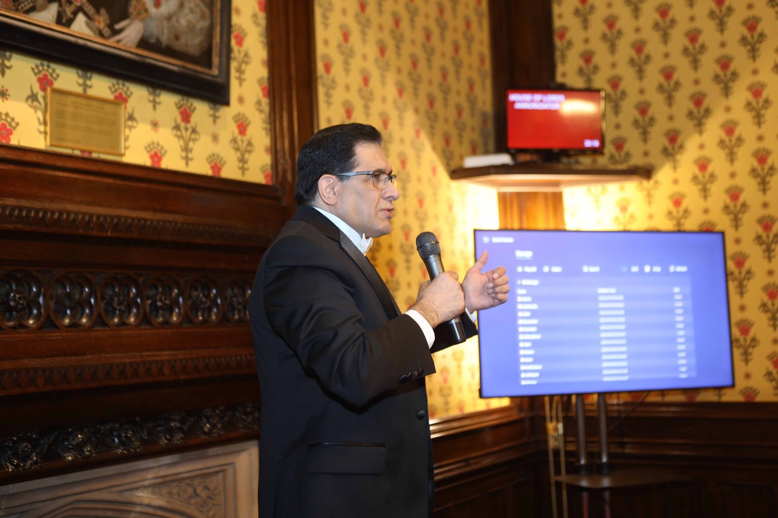 A speaker presents to the room beside the screen at the London ceremony